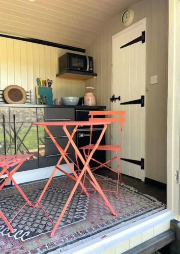 a kitchen with a red table in front of a door at The Rookery in Lothersdale