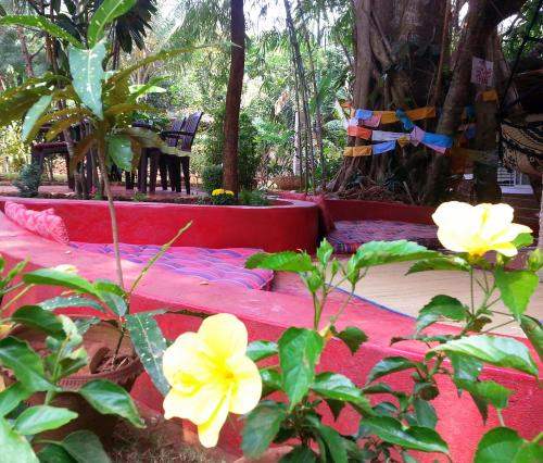 a red bed in a garden with yellow flowers at Namaste Yoga Farm in Gokarna