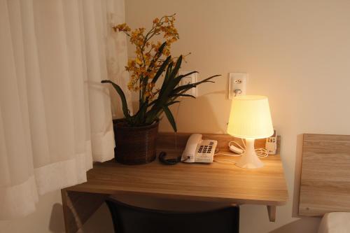 a table with a lamp and a phone and a plant at Turis Hotel Centro in Campo Grande