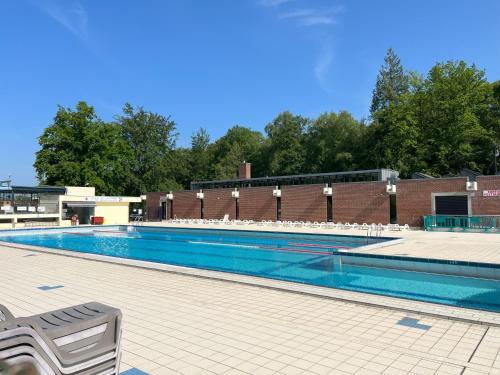 une piscine avec des chaises blanches et un bâtiment en briques dans l'établissement Manoir de la Prise Tarot, à Bagnoles-de-l'Orne
