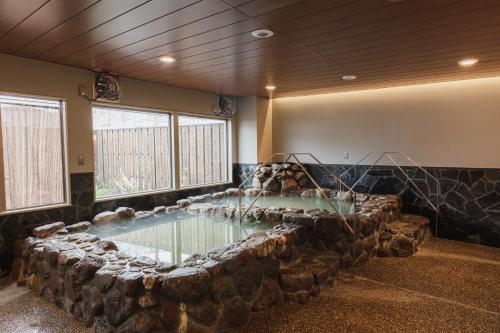 a large rock lined pool in a room with a stone wall at Hotel Arthur KITAHAMA BASE in Beppu