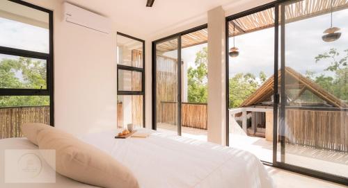 une chambre avec un lit blanc et de grandes fenêtres dans l'établissement Villa Toh, à Tulum