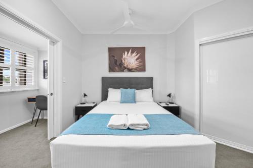 a white bedroom with a large bed with two towels at CocoBrew Boutique Apartments in Rockhampton
