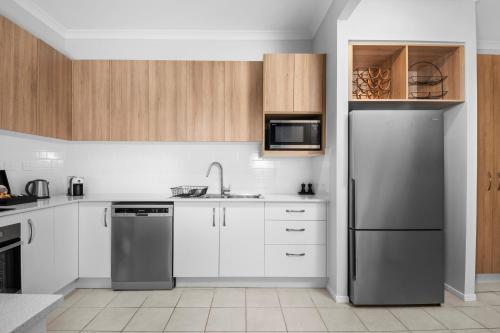 a kitchen with white cabinets and a stainless steel refrigerator at CocoBrew Boutique Apartments in Rockhampton