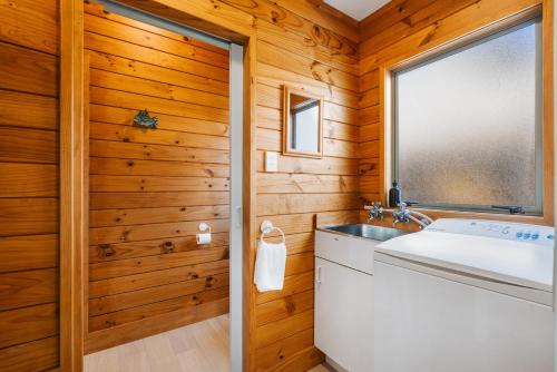 baño con paredes de madera, lavabo y ventana en The Iconic Kiwi Bach, Full Site Downtown Mount, en Mount Maunganui