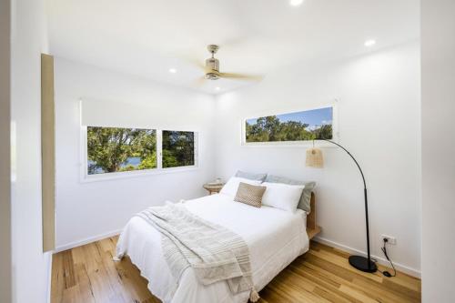 ein weißes Schlafzimmer mit einem Bett und zwei Fenstern in der Unterkunft Aura Apartment-LJHooker Yamba in Yamba