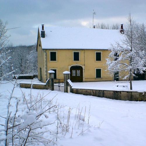 une maison jaune dans la neige avec une cour recouverte de neige dans l'établissement Au Moulin des Fées - Maison d'hôtes Cascades du Hérisson, à Bonlieu