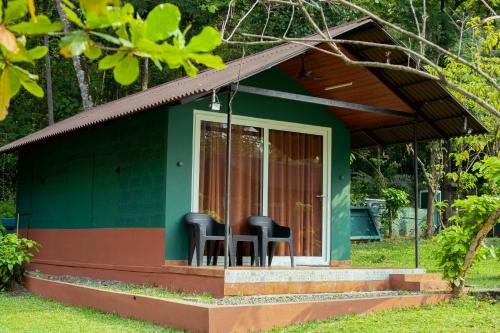 a small green house with two black chairs on the porch at The Nest Thattekad in Thattakād