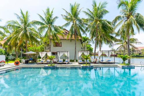 a swimming pool in front of a villa with palm trees at Hoi An Beach Resort in Hoi An