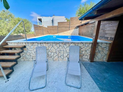 two chairs and a swimming pool with a stone wall at Apartmani Jasminka in Dramalj