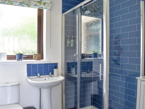 een blauwe betegelde badkamer met een wastafel en een douche bij Failte in Gamrie