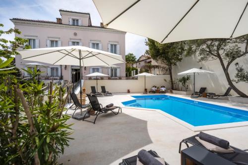 a pool with chairs and umbrellas next to a house at Villa Cassia in Mali Lošinj