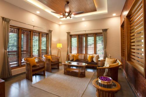 a living room with couches and chairs and windows at Regal Retreat by VEO - Part of StayVista in Wayanad