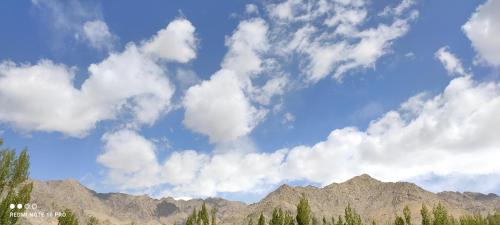 a cloudy sky with mountains and trees in the foreground at Noor Guest House in Leh