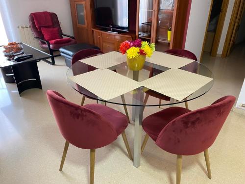 una mesa de cristal con sillas rojas y una mesa con flores. en Apartamentos Alcañiz, Silvia en Alcañiz