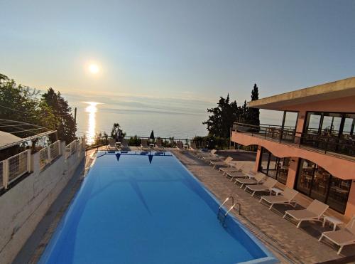 a large swimming pool with lounge chairs and the sunset at Siora Leni Hotel in Benitses