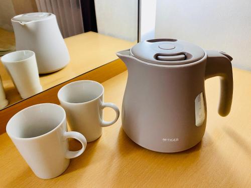 a tea kettle and two cups on a table at Valie Hotel Hiroshima in Hiroshima