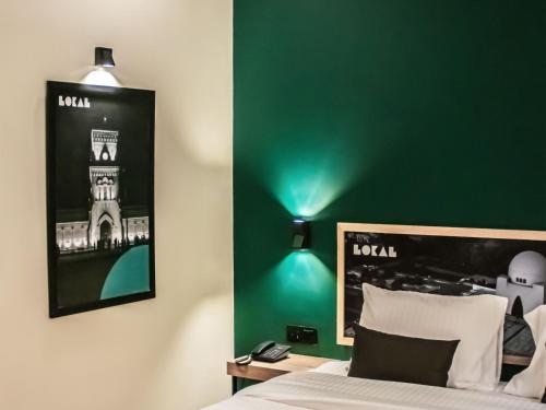 una camera da letto con una parete verde, un letto e una lampada di LOKAL Rooms x Shahrah-e-Faisal (Nursery) a Karachi