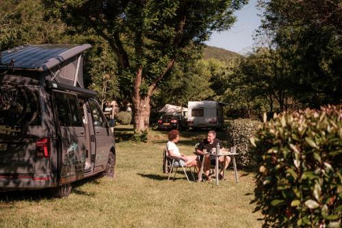 two people sitting at a table in front of a van at Slow Village Anduze - Cévennes in Corbés
