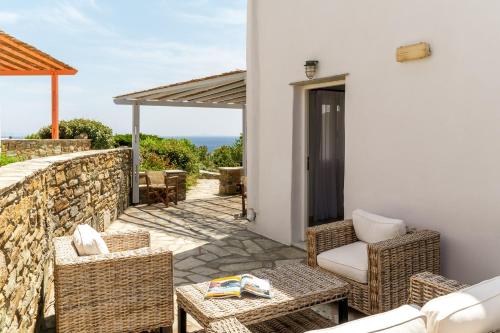 a patio with wicker chairs and tables and a stone wall at Anemologio 301 Tinos in Agios Ioannis Tinos