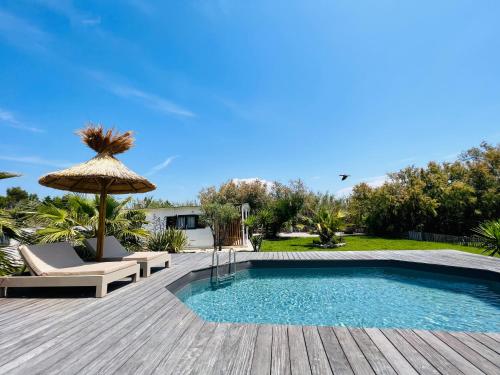 una piscina con terraza y sombrilla en Cabane le Flamant avec jardin, piscine chauffée et parking en Saintes-Maries-de-la-Mer