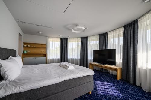 a hotel room with a bed and a flat screen tv at Roze Village Jūrnieka Ligzda in Pērkone