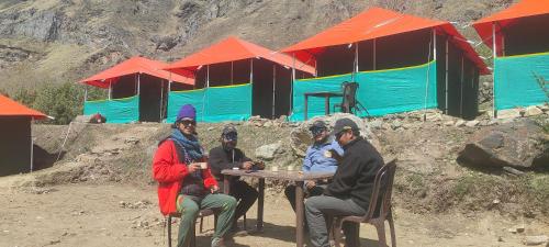 eine Gruppe von Personen, die vor Zelten an einem Tisch sitzen in der Unterkunft Buddy Hikers Stay Badrinath in Badrīnāth