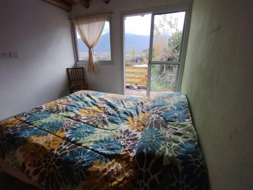 a bed with a colorful comforter in a bedroom with a window at Vista los Andes in Cacheuta