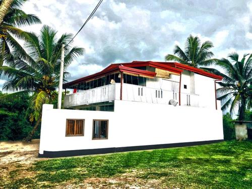 a white house with a red roof and some palm trees at Villa Sanitha in Ambalangoda