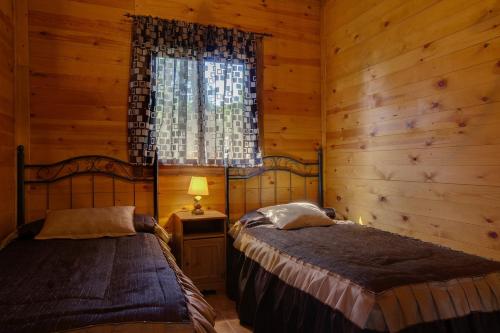 two beds in a room with wooden walls and a window at Apartamentos Rurales Sierra Luna in Andújar