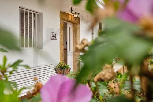 a white building with a door with a window and purple flowers at Casona del Sol El Retorno I in Lastres