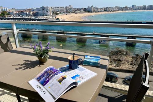 - une table avec un journal et une vue sur la plage dans l'établissement Lumineux & Vue exceptionnelle Parking, à Les Sables-dʼOlonne