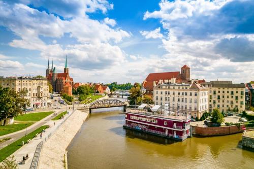 a river in a city with buildings and a boat at Great Polonia River Boat Apartments Wrocław in Wrocław