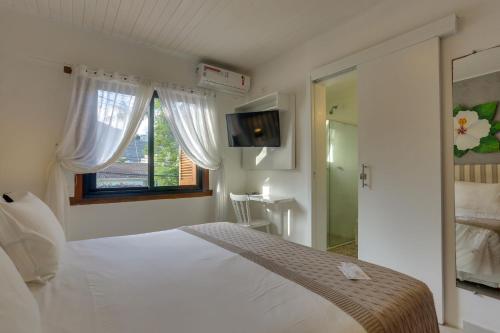 a white bedroom with a bed and a window at Chez Louise et Louis Pé na Areia in Juquei