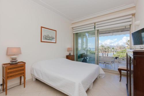 a white bedroom with a bed and a balcony at SERRENDY Sea View Cannes Croisette in Cannes