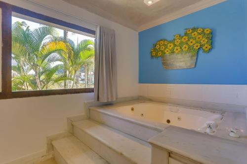 a bathroom with a tub and a window with a potted plant at Chez Louise et Louis Pé na Areia in Juquei