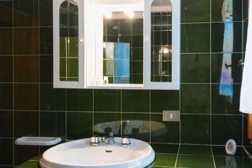 Baño de azulejos verdes con lavabo y espejo en Casa Ginepro en Olbia