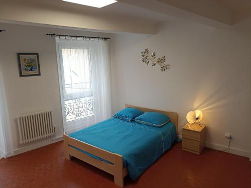 1 dormitorio con cama con sábanas azules y ventana en La Maison de la Cloche, en Puimoisson