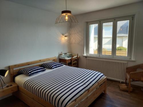 ein Schlafzimmer mit einem Bett mit gestreifter Bettwäsche und einem Fenster in der Unterkunft Maison au cœur du bourg, plages à pied in Plougasnou