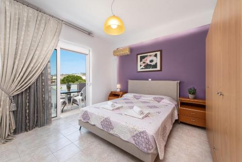 a bedroom with a bed with purple walls and a balcony at Savvas Apartment in Afantou