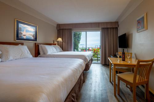 a hotel room with two beds and a desk and a window at Sidney Waterfront Inn & Suites in Sidney