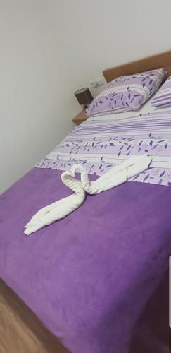 a bed with purple and white sheets and pillows at Apartmani Kate in Klek