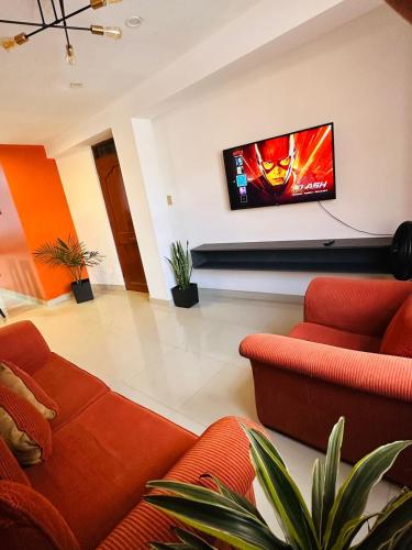 a living room with orange furniture and a flat screen tv at Castellares la Puebla Hostelería Departamento in Ayacucho