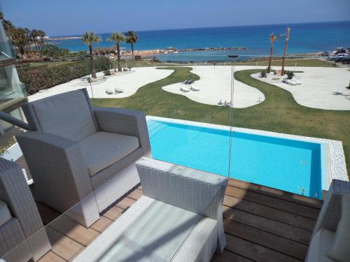 a patio with a pool and chairs and the ocean at Thalassa Court Sandy Beach Apartment in Protaras