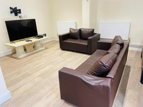 a living room with a leather couch and a television at Glory House in Ilford