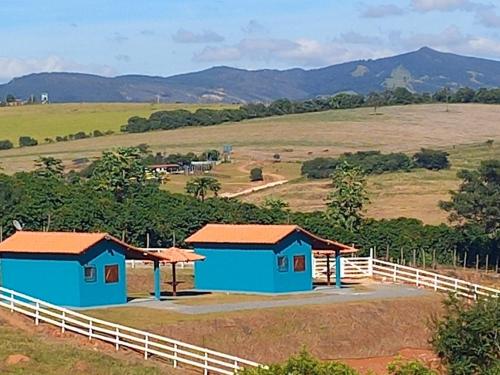 deux cottages bleus dans un champ avec une clôture dans l'établissement Chales Horizonte das Pedras, à São Thomé das Letras