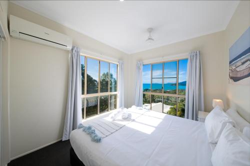1 dormitorio con 1 cama blanca grande y ventanas grandes en The Power House - Views & More en Airlie Beach