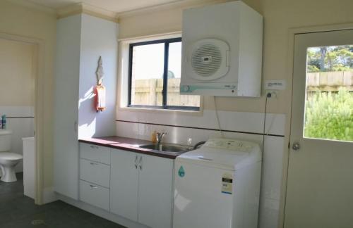 eine weiße Küche mit einem Waschbecken und einem Fenster in der Unterkunft 526 Arthur Kaine Dr Merimbula in Merimbula
