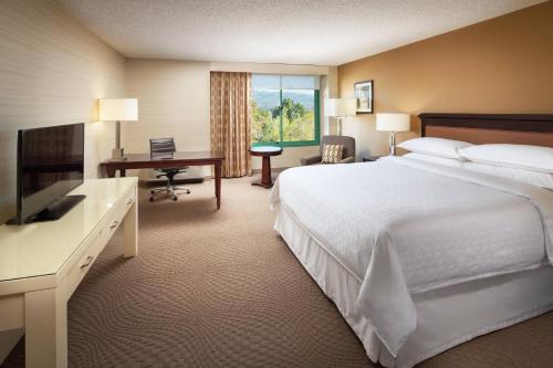 a hotel room with a bed and a desk and a television at Sheraton San Jose in Milpitas