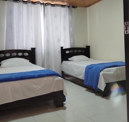 a bedroom with two beds and a window with curtains at La posada del gordo in Quimbaya